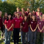 Gruppenfoto der gewählten Schul- und Stufensprecherinnen und -sprecher zusammen mit der Verbindungslehrerin Frau Wörner. Die Gruppe von etwa 17 Personen steht draußen auf einer Wiese vor grünen Bäumen und blauem Himmel. Fast alle tragen einheitliche dunkelrote T-Shirts mit einem weißen Logo auf der Brust, um ihren Zusammenhalt als Team zu zeigen.